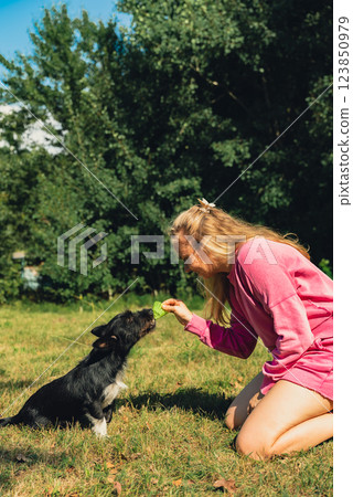 Pretty pet owner playing with dog Neon yellow badminton shuttlecock on green grass outdoors. Alternative fitness recreational sport. Furry friends pet-centric 123850979