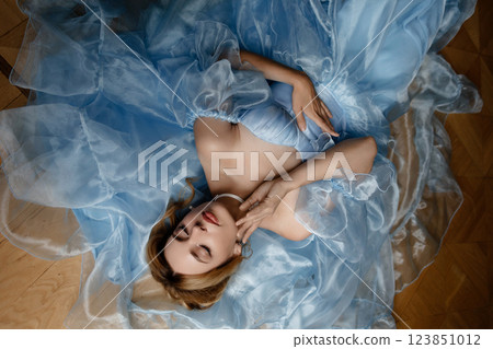 Elegant woman in light blue ball gown posing lying on the floor. Top view. 123851012
