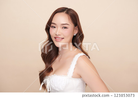 A beautiful young Asian woman with clean, fresh skin against a beige background. She represents beauty, skincare, and spa treatments. 123853073