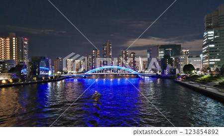 A motorboat is heading towards the night view of the blue-lit Eitai Bridge across the Sumida River and skyscrapers. 123854892
