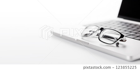 Closeup of an office table featuring a sleek laptop and reading glasses on a clean white surface 123855225
