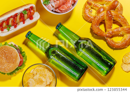 A vibrant photo showcasing bottles of beer surrounded by various snacks and fast food 123855344