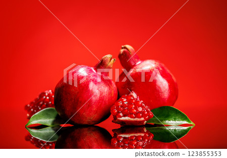 A ripe, glossy pomegranate placed against a vibrant red background 123855353