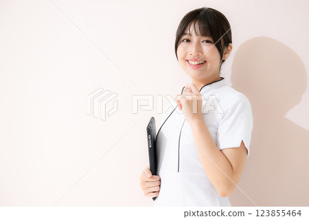 美容師或美容護士手持平板電腦以接待或諮詢姿勢的正面視圖粉紅色背景 美容師或美容護士手持平板電腦以接待或諮詢姿勢的正面視圖粉紅色背景 123855464