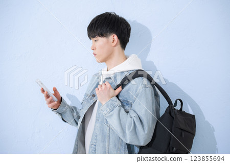 The upper body of a young man in his 20s smiling and tapping on a smartphone The upper body of a young man in his 20s smiling and tapping on a smartphone 123855694