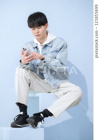Full body of a young man in his 20s holding a smartphone and tapping with a smile, vertical Full body of a young man in his 20s holding a smartphone and tapping with a smile, vertical 123855699