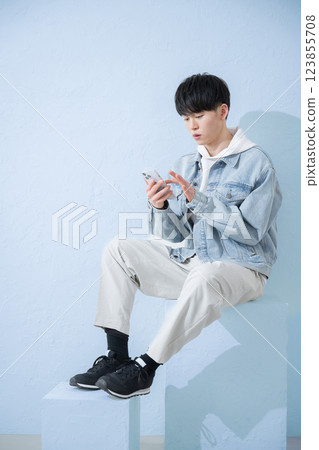 The upper body of a young man in his 20s holding a smartphone, smiling and tapping with his head down 123855708