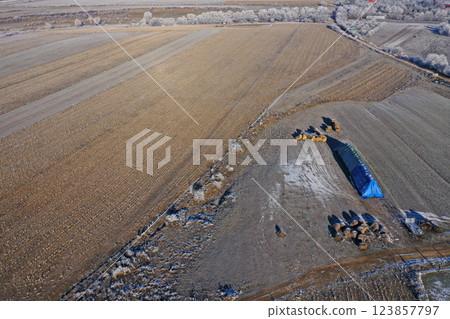 Aerial view of rural landscape showing farm fields, icy terrain, and distant village during winter morning Aerial view of rural landscape showing farm fields, icy terrain, and distant village during winter morning 123857797