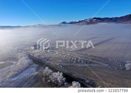 Aerial view of snow-covered landscape with fog rolling over fields and hills in winter season Aerial view of snow-covered landscape with fog rolling over fields and hills in winter season 123857798