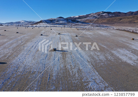 Aerial view of snow-covered field dotted with hay bales under a clear blue sky during winter Aerial view of snow-covered field dotted with hay bales under a clear blue sky during winter 123857799