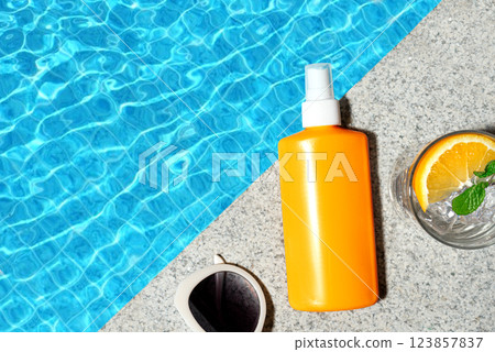 Sunscreen lotion and cocktail drink near pool water Sunscreen lotion and cocktail drink near pool water 123857837