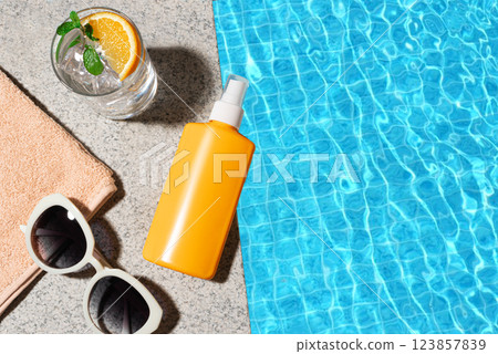 Sunscreen bottle and cocktail drink near pool water 123857839