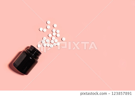 White pills spilling from black container on pink background 123857891