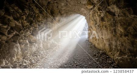 Light beams entering dark stone cave tunnel inspiring hope and faith 123858437