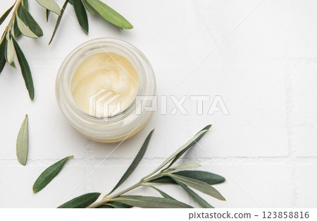 Moisturizing cream surrounded by olive branches on white surface Moisturizing cream surrounded by olive branches on white surface 123858816