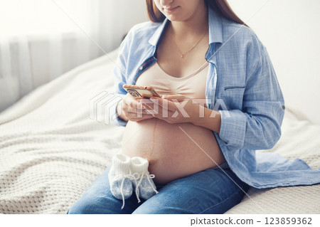 A pregnant woman is seen resting comfortably on bed, holding a pair of baby shoes near her belly. She appears content and serene, enjoying a quiet moment A pregnant woman is seen resting comfortably on bed, holding a pair of baby shoes near her belly. She appears content and serene, enjoying a quiet moment 123859362