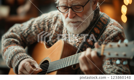 An elderly man with glasses and a warm sweater plays an acoustic guitar in a cozy setting, enjoying a peaceful moment. 123860148