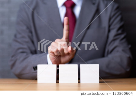 Three white wooden blocks and a middle-aged male businessman pointing his index finger up Three white wooden blocks and a middle-aged male businessman pointing his index finger up 123860604