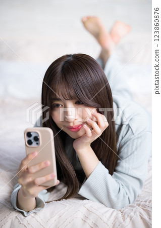 Smiling woman lying on the bed and holding a smartphone, portrait 123860876