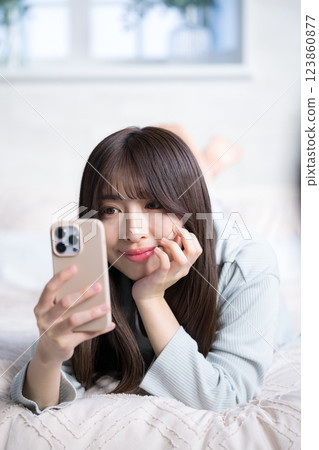 Smiling woman lying on the bed and holding a smartphone, portrait Smiling woman lying on the bed and holding a smartphone, portrait 123860877