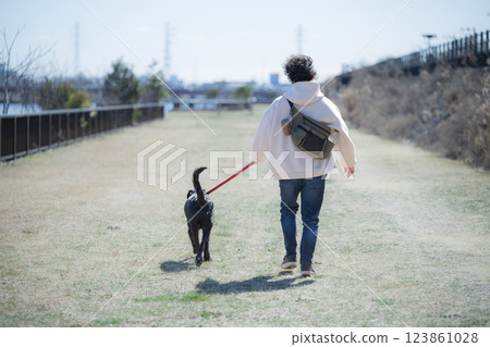 A man walking a large dog in a park on a riverbank, faceless back view 123861028