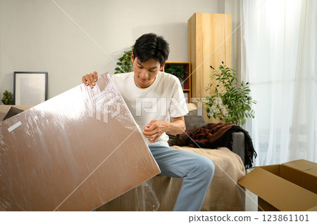 Young man unwrapping new furniture piece preparing to assemble in a stylish home 123861101