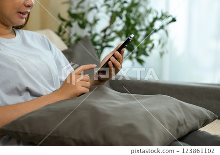 Smiling young woman sitting on a couch and checking social media on smartphone 123861102