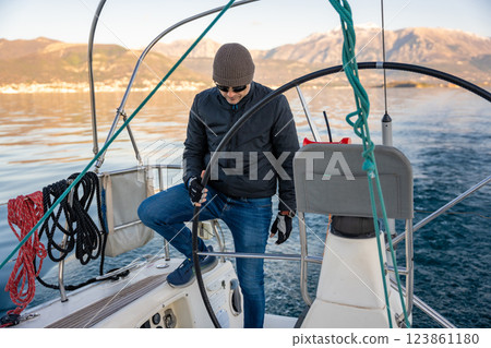 Young man captain standing at the helm and controls a sailboat during a journey by sea in winter time in Montenegro Young man captain standing at the helm and controls a sailboat during a journey by sea in winter time in Montenegro 123861180