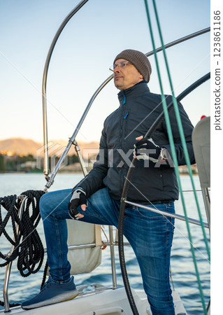 Young man captain standing at the helm and controls a sailboat during a journey by sea in winter time in Montenegro Young man captain standing at the helm and controls a sailboat during a journey by sea in winter time in Montenegro 123861186