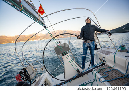 Young man captain standing at the helm and controls a sailboat during a journey by sea in winter time in Montenegro 123861193
