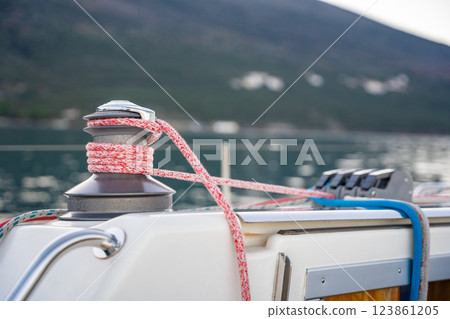 Close-up of a yacht winch with red and blue ropes secured, set against the scenic backdrop of the Bay of Kotor. Concept of sailing, nautical adventure, and maritime lifestyle Close-up of a yacht winch with red and blue ropes secured, set against the scenic backdrop of the Bay of Kotor. Concept of sailing, nautical adventure, and maritime lifestyle 123861205