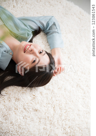 Aerial view of a young woman lying on her back in a room with a smile, looking at the camera, relaxing or taking a nap, wide angle 123861543