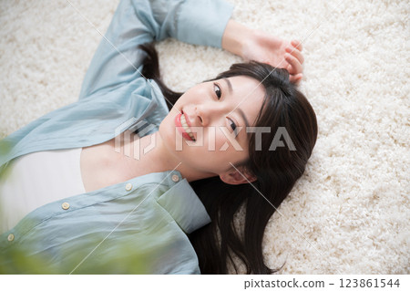 Aerial view of a young woman lying on her back in a room with a smile, looking at the camera, relaxing or taking a nap, wide angle 123861544