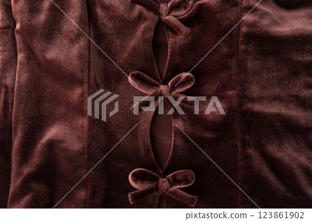 Close-up of brown velvet fabric featuring three decorative bows and cut-out details.  123861902