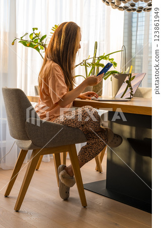 Woman working from home office with smartphone and laptop in a cozy, sunlit in homewear in Prague 123861949