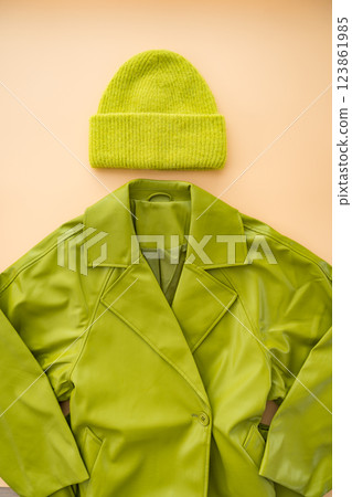 Flat lay of green faux leather coat , cashmere hat made from recycled materials on beige background. 123861985