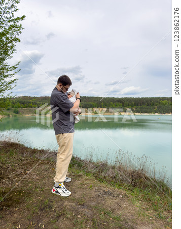 Father Holding Baby by Tranquil Lake 123862176