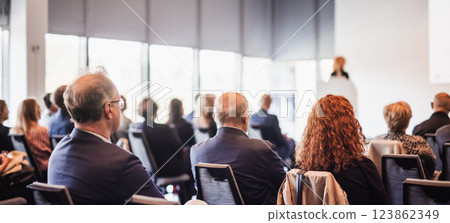 Business and entrepreneurship symposium. Female speaker giving a talk at business meeting. Audience in conference hall. Rear view of unrecognized participant in audience. Business and entrepreneurship symposium. Female speaker giving a talk at business meeting. Audience in conference hall. Rear view of unrecognized participant in audience. 123862349