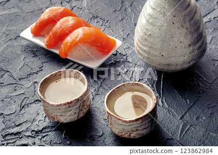 Sake in a pitcher and ochoko, traditional cup, with salmon nigiri Sake in a pitcher and ochoko, traditional cup, with salmon nigiri 123862984