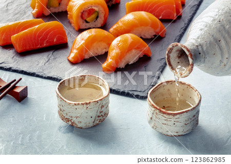 Sake poured into ochoko, traditional cup, with salmon nigiri and sashimi 123862985