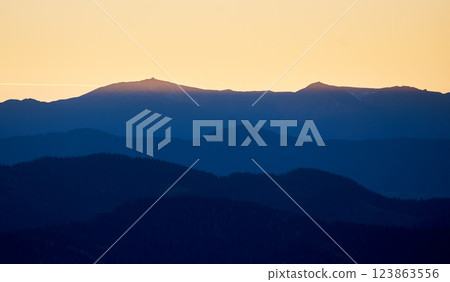 Silhouette of distant mountains at sunset, with golden sky transitioning into deep blue shadows. Ridges and peaks create stunning contrast against warm hues of horizon. Silhouette of distant mountains at sunset, with golden sky transitioning into deep blue shadows. Ridges and peaks create stunning contrast against warm hues of horizon. 123863556