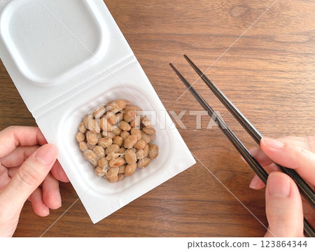 女人的手拿著一包納豆，桌上放著筷子 123864344