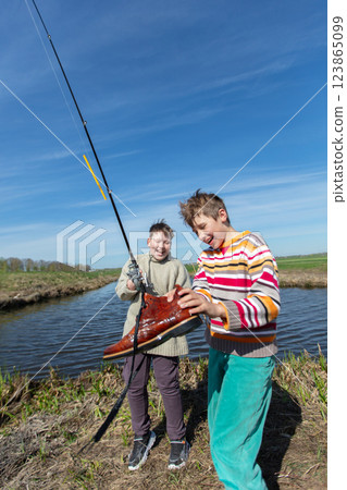 Funny fishing. Two of the boy's friends hooked an old shoe with a fishing rod and are laughing. Funny fishing. Two of the boy's friends hooked an old shoe with a fishing rod and are laughing. 123865099