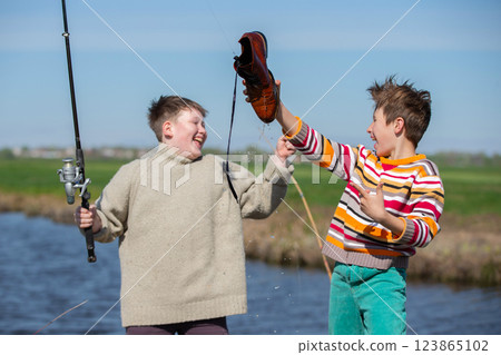 Funny fishing. Two of the boy's friends hooked an old shoe with a fishing rod and are laughing. Funny fishing. Two of the boy's friends hooked an old shoe with a fishing rod and are laughing. 123865102