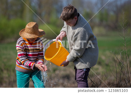 Two boys wash their hands by pouring water from a bucket. 123865103