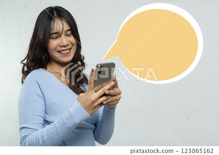 A girl standing replying to a message on her mobile phone with a smile, use of long hair woman advertising with talk box isolated on orange space A girl standing replying to a message on her mobile phone with a smile, use of long hair woman advertising with talk box isolated on orange space 123865162