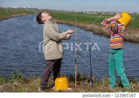 Funny photo of fishermen. Two boys are fishing and having fun. One of them put a bucket on his head. Funny photo of fishermen. Two boys are fishing and having fun. One of them put a bucket on his head. 123865167