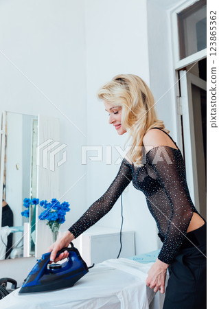 blonde woman ironing things on ironing board 123865362