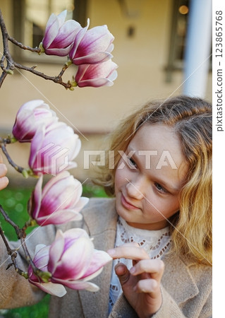 Blonde teenager girl looking at blooming magnolia flower 123865768