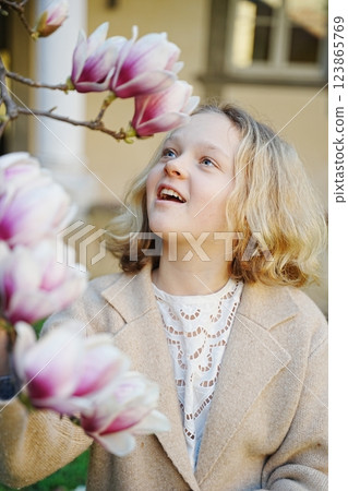Blonde teenager girl looking at blooming magnolia flower 123865769